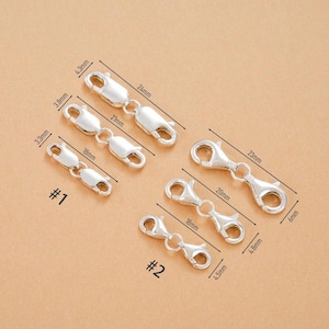May include: Several silver-colored lobster claw clasps of varying sizes are arranged on a light brown surface. Measurements are provided in millimeters, with the largest clasp measuring 24mm in length. The clasps are labeled #1 and #2.