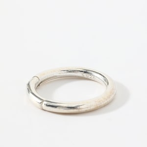 May include: A silver ring with a circular design. The ring has a textured surface and a clasp. The ring is marked with the number "925".