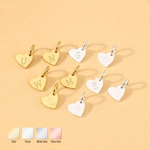 Puede incluir: Una colección de colgantes en forma de corazón con grabados de letras individuales. Los colgantes están disponibles en tonos dorados y plateados, cada uno con un pequeño lazo para sujetar. Las letras incluyen U, N, G, A, W, M, E, Q, H y J.