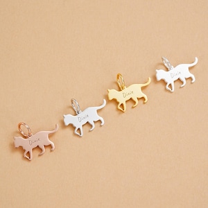 Op de afbeelding: Vier metalen katvormige bedels in roségoud, zilver en goudtinten. Elke bedel heeft een kleine lus aan de bovenkant en de naam "Dixie" gegraveerd op het lichaam van de kat. De bedels worden gepresenteerd op een neutrale achtergrond.