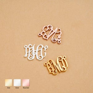 May include: Three monogram pendants in gold, silver, and rose gold. The pendants feature ornate, intertwined letters. The gold pendant displays the letters "BM", the silver pendant displays "HH", and the rose gold pendant displays "MN".