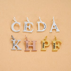 Könnte beinhalten: Acht Buchstabenanhänger aus Metall mit Biegeringen, angeordnet in zwei Reihen. Die obere Reihe zeigt die silbernen Buchstaben C, E, D und A, graviert mit den Namen Eachus, Danielle und Alice. Die untere Reihe enthält K, H, P und F in verschiedenen Farben.