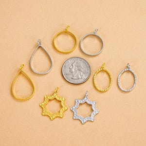 以下が含まれることがあります： さまざまな形状の金と銀色のジュエリーペンダントのコレクション。涙型、円、スターバーストなど。一部のペンダントには、小さな透明な宝石が飾られています。サイズの目安として、米国の25セント硬貨が含まれています。