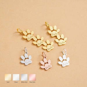 Peut inclure: Des breloques en forme de pattes de chien en or, argent, or blanc et or rose, gravées du nom "Bella". Les breloques ont la forme d'une patte et sont dotées d'une petite boucle pour les attacher. Mesures en cm.