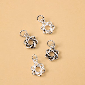 May include: Four silver charms with a looped, star-like design. Each charm has a small loop at the top for attaching to a chain or other jewellery component. The charms are displayed on a light brown surface.