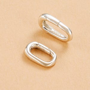 May include: Two oval silver clasps with a polished finish, connected by a hinge. The clasps are made of a shiny metal and are set against a neutral background. The clasps are marked with "S925".