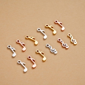 Peut inclure: Une collection de petits charms en forme de notes de musique métalliques, de couleurs argent, or et or rose. Les breloques sont dispersées sur une surface de ton neutre, mettant en valeur leur design détaillé et leur finition brillante. Idéal pour la création de bijoux.