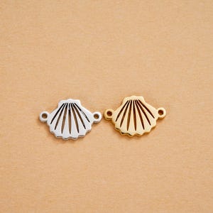 Op de afbeelding: Twee schelpbedels, één zilverkleurig en één goudkleurig, worden getoond tegen een neutrale achtergrond. Elke bedel heeft een gedetailleerd schelpenontwerp met uitstralende lijnen en kleine lussen voor bevestiging, perfect voor het maken van sieraden.