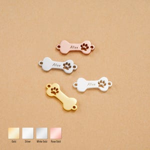 May include: Four bone-shaped pet tags in gold, silver, white gold, and rose gold. Each tag has a paw print and the name "Alice" engraved. The tags are displayed on a neutral background.