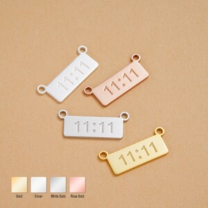May include: Four rectangular charms in gold, silver, white gold, and rose gold. Each charm has the engraved text "11:11" and two small loops for attaching to jewelry. The charms are displayed on a neutral background.