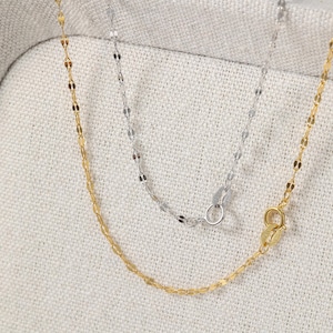 May include: Two delicate necklaces. One is gold-colored, the other is silver-colored. Both have a delicate chain design with small, oval-shaped links. The gold necklace has a lobster clasp, and the silver necklace has a spring ring clasp.