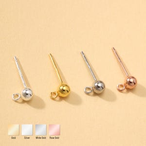 Könnte beinhalten: Vier Ohrstecker in Gold, Silber, Weißgold und Roségold. Jeder Stecker hat eine kleine Kugel und eine Schlaufe zum Anbringen eines Anhängers. Das Bild enthält Farbfelder mit den Namen der Metallfarben.