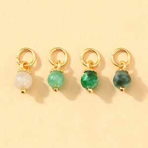 May include: Four gold-colored charms with gemstone beads. The beads are in shades of white, light green, and dark green. Each charm has a small gold loop at the top and a gold bead at the bottom.