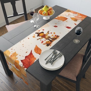 Può includere: Runner da tavolo a tema autunnale con un design di spaventapasseri, zucche e foglie cadenti nei toni dell'arancione, rosso e marrone. Il runner è posizionato su un tavolo di legno scuro, con piatti, posate e calici.