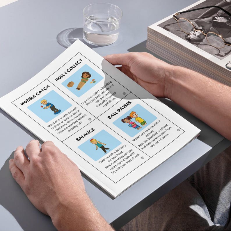 May include: A person holding a white printed sheet with illustrated instructions for balance and coordination exercises. The sheet features colorful drawings and text, including "Wobble Catch," "Roll & Collect," "Balance," and "Ball Passes."