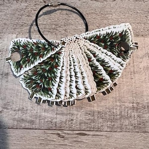 May include: A set of 12 Christmas tree-shaped paper punch-outs, each with a green and red design, attached to a black ring.