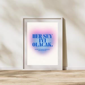 May include: A framed art print with a white border. The artwork features a gradient background of pink and blue hues. Bold blue text reads "HER SEY IYI OLACAK." Below, smaller text is visible.
