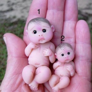 May include: Two small, realistic baby dolls made of polymer clay. The dolls are nude and have painted features. The dolls are numbered 1 and 2.
