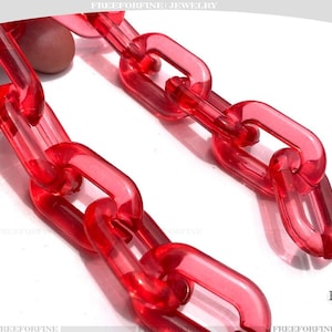 May include: Close-up of a translucent red chain with rectangular links. The chain is made of a clear material, and the links are connected to each other. The jewelry is set against a white background.