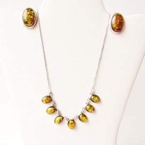 K&ouml;nnte beinhalten: Ein silbernes Halsketten- und Ohrring-Set. Der Schmuck besteht aus oval geformten Bernsteinen mit einer silbernen Fassung. Die Halskette hat eine Reihe von Bernsteinen, die den Ausschnitt hinunterlaufen. Die Ohrringe sind oval geformte Bernsteine.