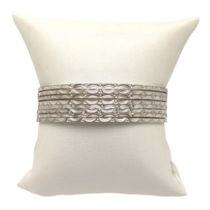 May include: A set of silver bangles with a decorative pattern. The bangles are stacked on a white pillow.