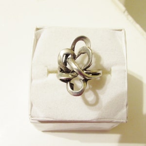 May include: A silver ring with a knot design. The ring is displayed on a white background.