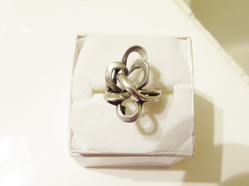 May include: A silver ring with a knot design. The ring is displayed on a white background.