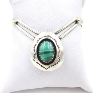 Op de afbeelding: Een zilveren armband met een groene malachiet steen gezet in een zilveren bezel. De armband heeft een V-vormig ontwerp en is gemaakt van sterling zilver.