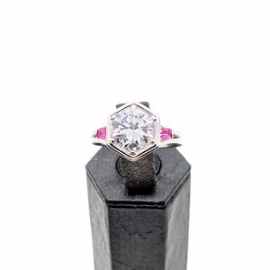 May include: A silver ring with a large, clear, hexagonal-shaped diamond and three small pink stones on the band.