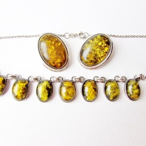 K&ouml;nnte beinhalten: Ein Schmuckset mit Halskette und passenden Ohrringen. Das Set besteht aus ovalen Bernsteinsteinen mit einer silberfarbenen Metalleinfassung. Die Bernsteinsteine haben eine goldgelbe Farbe mit sichtbaren Einschl&uuml;ssen. Die Halskette hat mehrere Bernsteinsteine.
