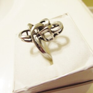 May include: A silver ring with a unique, abstract design. The ring is made of a single piece of metal that is twisted and turned to create a complex pattern.