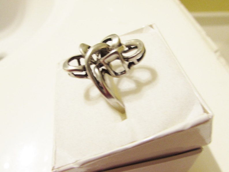 May include: A silver ring with a unique, abstract design. The ring is made of a single piece of metal that is twisted and turned to create a complex pattern.
