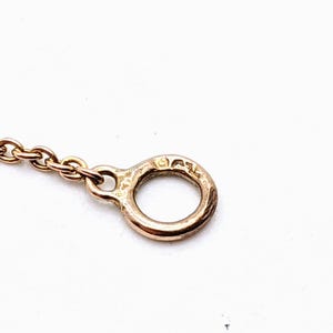 May include: Close-up of a gold chain with a round clasp. The clasp has a small inscription on it.