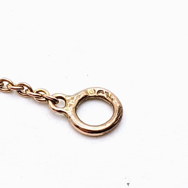 May include: Close-up of a gold chain with a round clasp. The clasp has a small inscription on it.