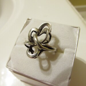 May include: A silver ring with a unique, abstract design. The ring is made of a single piece of metal that is twisted and turned to create a complex pattern.