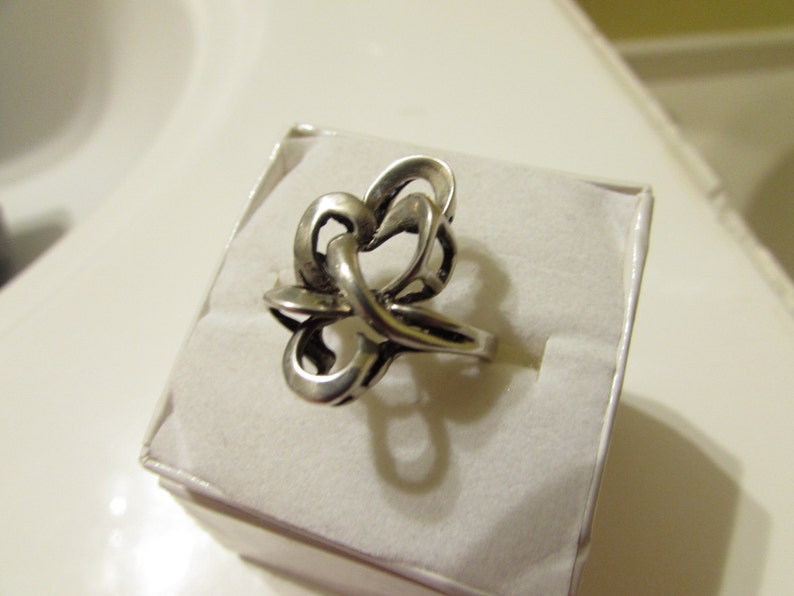 May include: A silver ring with a unique, abstract design. The ring is made of a single piece of metal that is twisted and turned to create a complex pattern.