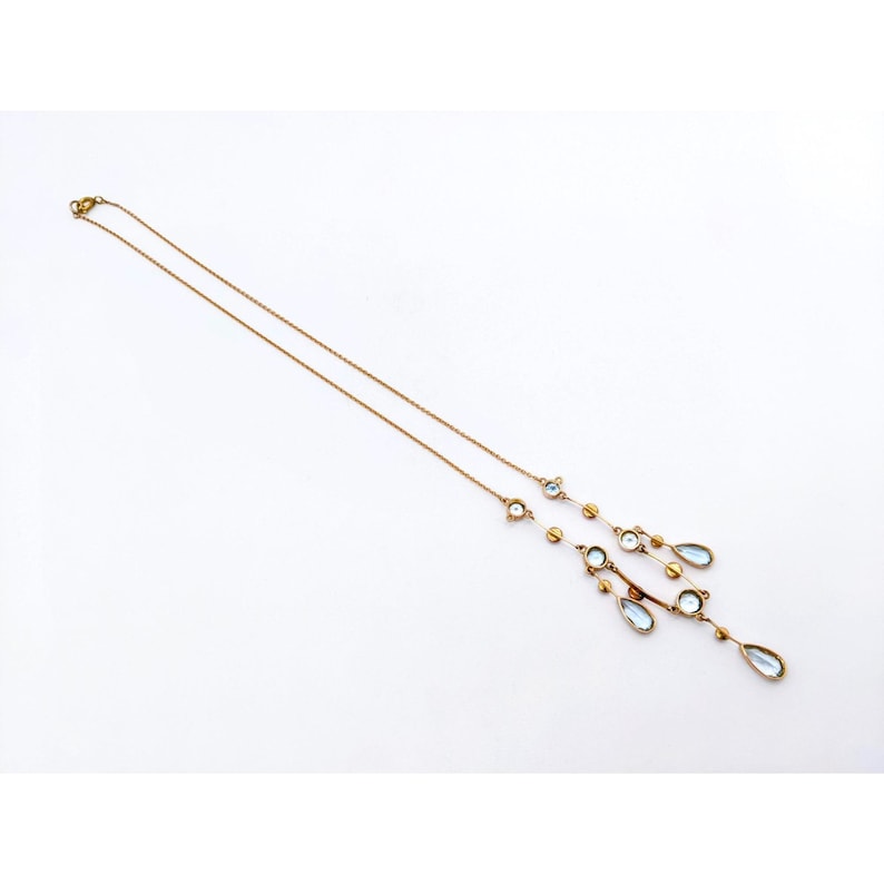 May include: A gold chain necklace with a pendant featuring multiple teardrop-shaped blue stones and small round gold beads.