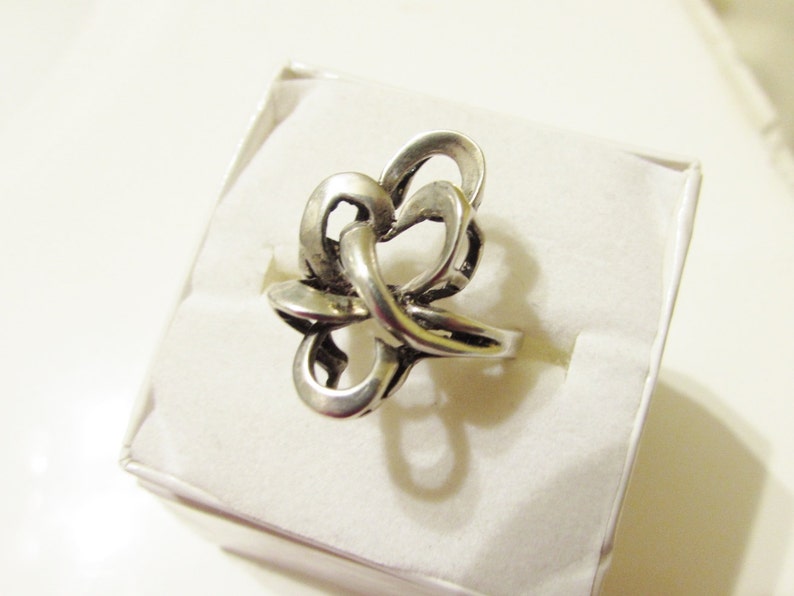 May include: A silver ring with a knot design. The ring is displayed on a white background.