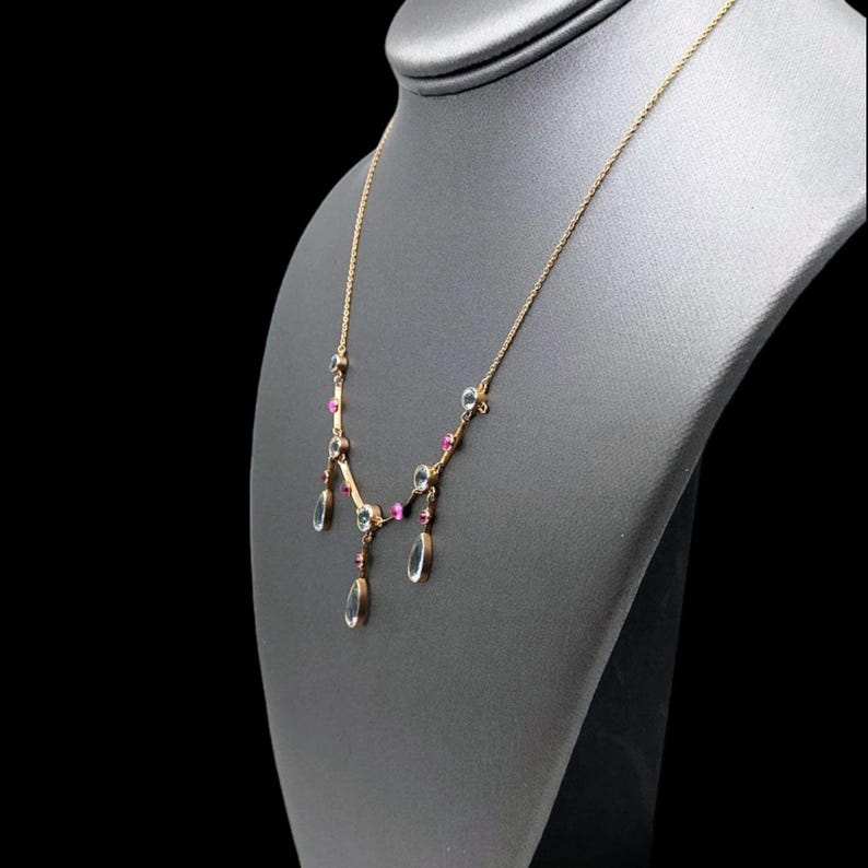 May include: A gold necklace with a delicate chain and teardrop-shaped clear glass stones accented with small pink stones.