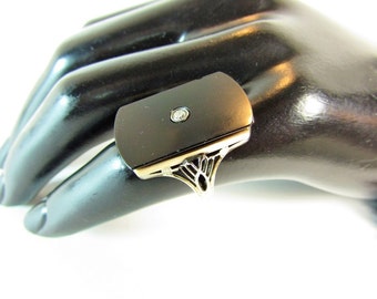May include: A black onyx ring featuring a single diamond set in a gold setting. The ring has a distinctive design with a decorative filigree pattern.