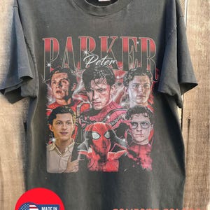 May include: Dark gray t-shirt featuring a graphic of Peter Parker from Spider-Man. The design includes the text "PARKER Peter" in red and white, with multiple images of the character. The shirt also has "COMFORT COLORS PEPPER" printed on it.