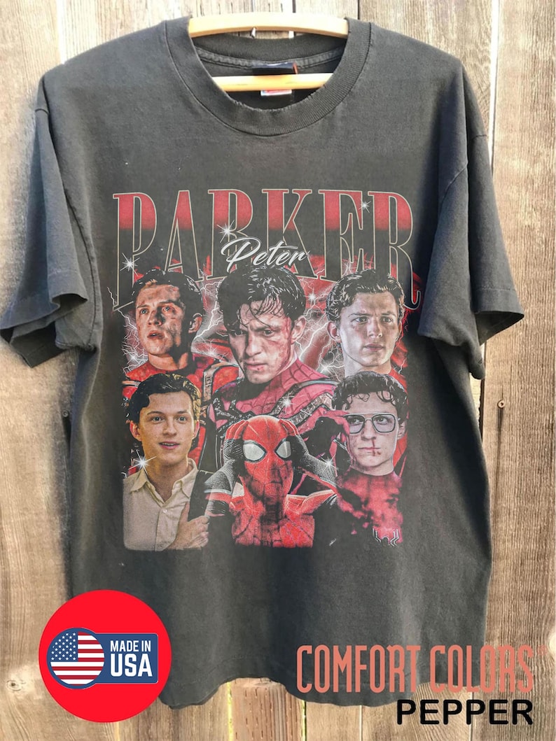 May include: Dark gray t-shirt featuring a graphic of Peter Parker from Spider-Man. The design includes the text "PARKER Peter" in red and white, with multiple images of the character. The shirt also has "COMFORT COLORS PEPPER" printed on it.