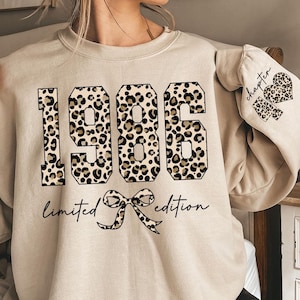 May include: A sand-colored sweatshirt with the year "1986" in large, leopard print numbers. Below the numbers is the text "limited edition" with a bow graphic. The left sleeve has the word "chapter" and a leopard print heart.