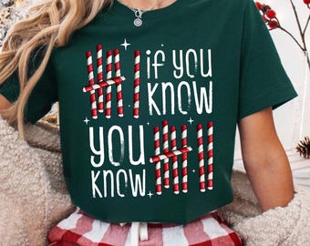 May include: A dark green t-shirt with the text "If you know, you know" in white. The text is designed with red and white candy cane stripes. The person is wearing red and white plaid pajama pants.
