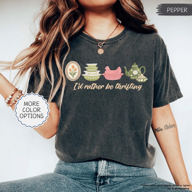 Pu&ograve; includere: T-shirt grigio scuro con la frase "I'd rather be thrifting" e illustrazioni di utensili da cucina vintage. Il design include un tulipano incorniciato, ciotole impilate, una gallina in un cestino e una teiera.