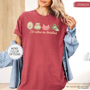 Pu&ograve; includere: T-shirt color cremisi con la scritta "I'd rather be thrifting" e una grafica di utensili da cucina vintage. La grafica include un ovale floreale, ciotole impilate, una gallina in un cestino e una teiera. La maglietta ha una vestibilit&agrave; ampia.
