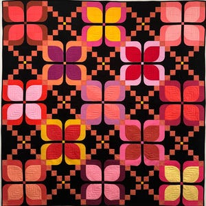 May include: A square quilt featuring a repeating pattern of stylised four-petal flowers in shades of red, pink, orange, and yellow. The flowers are set against a solid black background with a grid of small orange and pink squares between them.