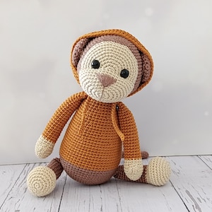 May include: A crocheted monkey toy wearing a brown hooded sweater. The monkey has brown eyes and a white face.