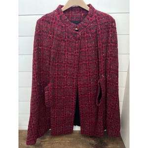 May include: A red and black patterned jacket with a round collar and two front pockets. The jacket is hanging on a wooden hanger against a white background. The jacket has a single wooden button closure.