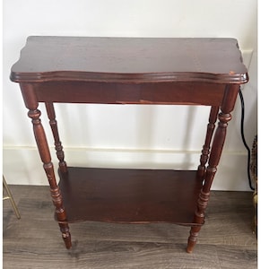 May include: A dark brown, antique-style side table with a scalloped top and a lower shelf. The table has turned legs and measures approximately 30 inches tall.